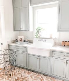 a kitchen with gray cabinets and a white sink in the center is surrounded by brick flooring