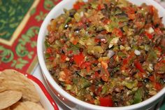 a white bowl filled with salsa next to tortilla chips on a red and green table cloth