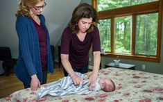 two women standing over a baby laying on a bed