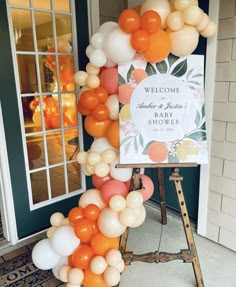 an orange and white balloon arch with welcome sign on the front door to a house