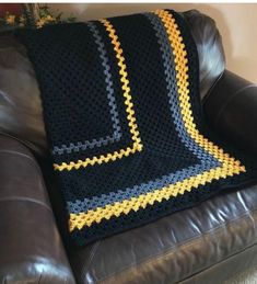 a crocheted blanket sitting on top of a brown couch next to a black leather chair