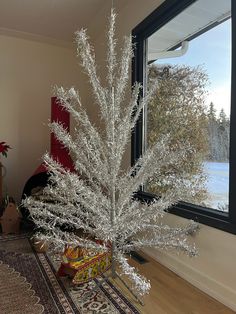 a white christmas tree sitting on top of a wooden floor next to a large window