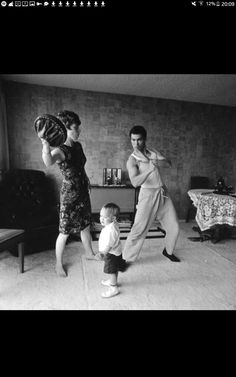 an old black and white photo of two people in a living room with a baby on the floor