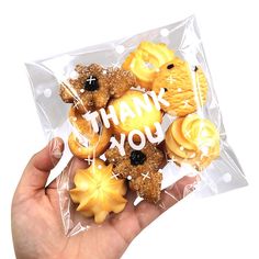 a hand holding a clear plastic bag filled with cookies and candies that say thank you