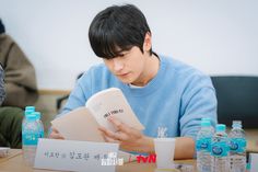 a man reading a book while sitting at a table with bottled water bottles around him