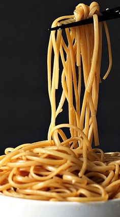 the noodles are being held by chopsticks in a white bowl with black background