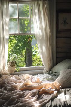 an unmade bed in front of a window with sheer curtains and flowers on it