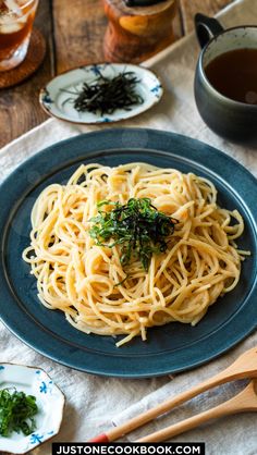 a blue plate topped with pasta and greens next to a cup of tea on top of a wooden table