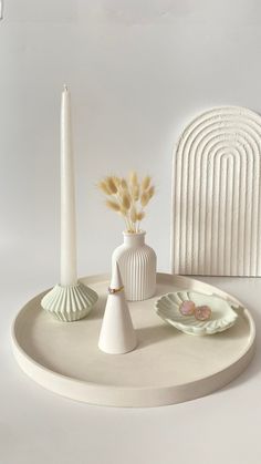 there is a white plate with two vases on it and a candle in the middle