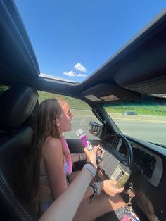 two women sitting in the driver's seat of a car, one holding a cell phone