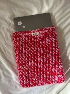 a laptop computer sitting on top of a red knitted cover over a white bed