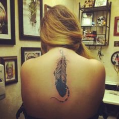 the back of a woman's neck with a feather tattoo on her left shoulder