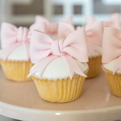 four cupcakes with pink bows are on a plate