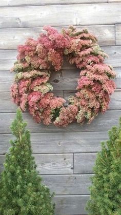 a wreath hanging on the side of a wooden wall next to some bushes and trees