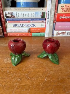 two red apples sitting on top of a wooden table next to books and coffee mug