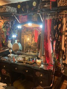 a dressing table with a mirror and lights on it in a room filled with clothes