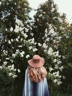 a woman standing in front of white flowers wearing a brown hat and ponchy