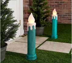 two teal candles sitting on top of green grass next to a potted tree