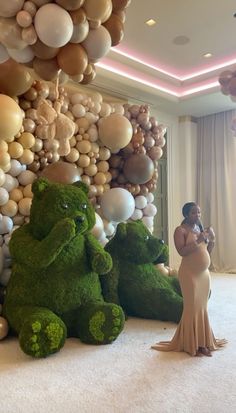 a woman standing next to a giant teddy bear in front of balloons on the wall