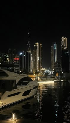 a white boat is docked in the water near some tall buildings at night with lights on