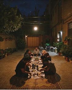 four people sitting at a table outside eating dinner in the dark, with lights on