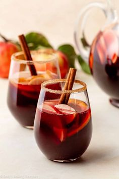 two glasses filled with apple cider and cinnamon sticks