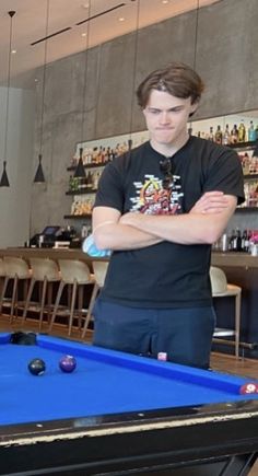 a man standing in front of a pool table with his arms crossed looking at the camera