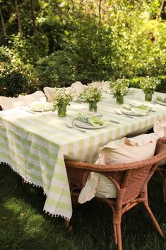 an outdoor table set up with plates and vases on top of it, surrounded by greenery