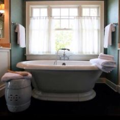 a bath tub sitting next to a window in a bathroom with white towels on it