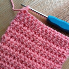 the crochet stitch is being worked on by a blue handled knitting needle, which sits next to a pink piece of yarn