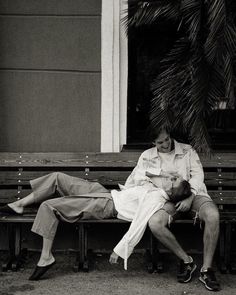 a man and woman sitting on a bench in front of a building with palm trees