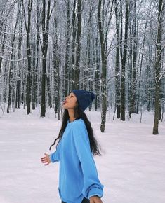 a woman standing in the snow with her arms out and looking up to the sky