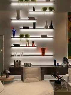 a living room filled with lots of white furniture and shelves above the couches covered in plants