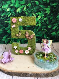 the letter e is made out of moss and has a fairy figurine next to it