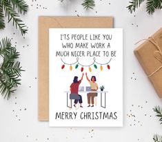 two people sitting at a table with christmas lights hanging from the ceiling, on top of a card that reads it's people like you who make work a much bigger place to be merry christmas