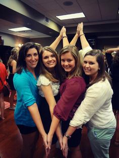 four young women are standing together in a room with their hands up to the ceiling