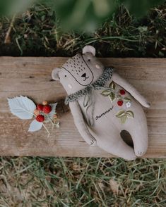 a teddy bear laying on top of a piece of wood with berries attached to it