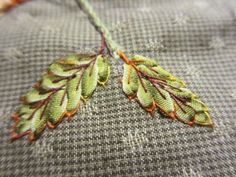 two green leaves are stitched together on a piece of fabric with orange thread in the middle