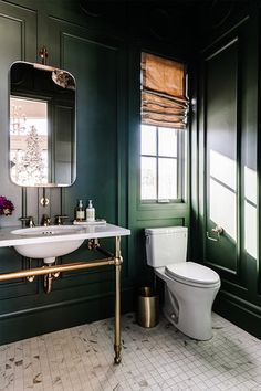 a bathroom with dark green walls and white tile flooring, along with a gold framed mirror on the wall