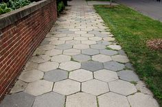 a brick wall next to a sidewalk with grass growing on it and bushes in the background