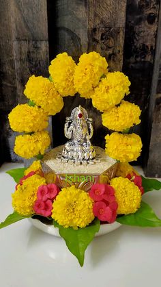 an arrangement of yellow and red flowers in front of a ganesh idol on a white plate