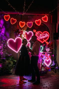 a man and woman standing in front of neon hearts