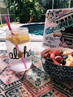 a bowl of fruit next to a jar of water on a table near a pool