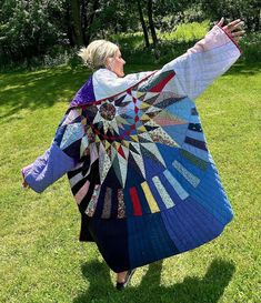 a woman is holding up a quilt in the grass with her arms out and hands outstretched