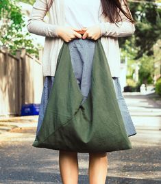 a woman is standing on the street holding a green bag with her hands behind her back