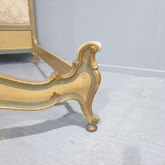 an antique bed frame with gold paint on the headboard and foot rests against a white wall