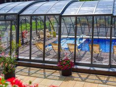 a large glass enclosed swimming pool in the middle of a garden with potted plants