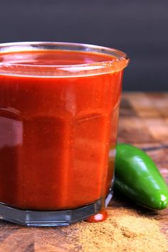 a jar of sauce sitting on top of a wooden table next to a green pepper