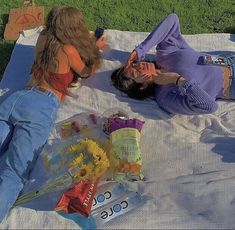 two women laying on a blanket in the grass with sunflowers and candy bags