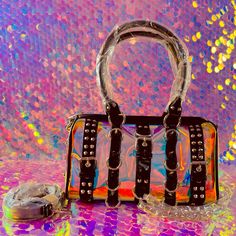 . This Mini Duffle Bag Has A Clear Holographic Vinyl Construction, Chain Detailing, Spiked And D-Ring Hardware, Top Handles, An Adjustable Shoulder Strap, And A Top Zipper Closure. Rainbow 100% Polyurethaneapprox. 10.5" W X 6.5" H X 4" D Edgy Rectangular Shoulder Bag For Party, Edgy Rectangular Bags With Detachable Strap, Edgy Rectangular Shoulder Bag With Hardware, Punk Party Bags With Adjustable Strap, Black Party Bag With Hardware Details, Black Party Bag With Hardware, Punk Rectangular Shoulder Bag For Party, Edgy Rectangular Shoulder Bag With Chain Strap, Punk Style Party Shoulder Bag With Adjustable Strap